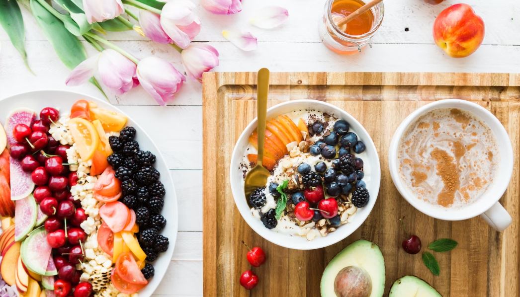 berries and other fruits in a bowl and plate with tulips in the background