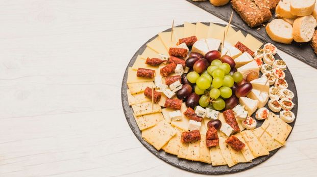 a close-up picture of a stone cheese board with smoked sausages and grapes