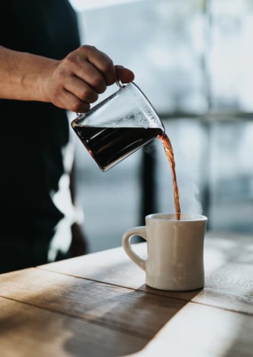 a hand pouring coffee into a cup from a small container