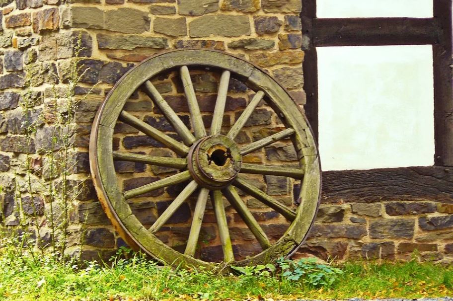 Image of a wooden cartwheel with a stone-brick wall as a background.