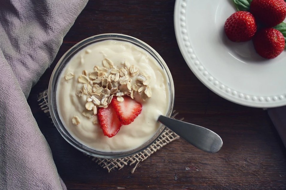 a bowl containing yogurt, oats, and strawberries; three strawberries on a plate