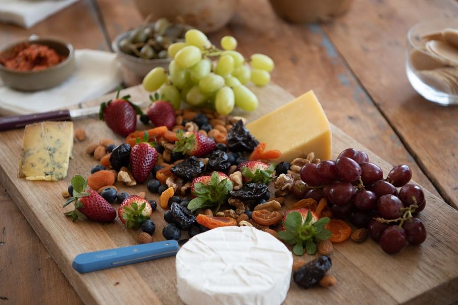 a cheese platter; a cheese board with lots of fruits and two chunks of cheese