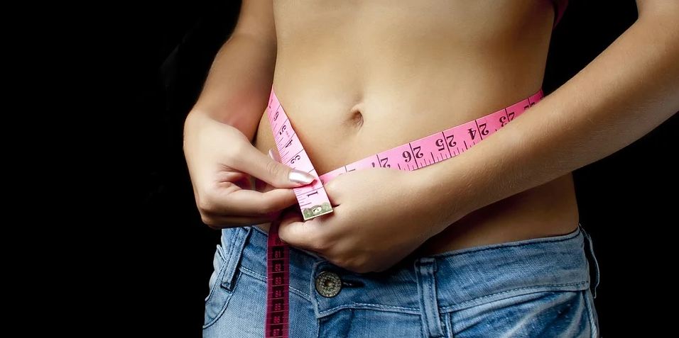 the image of a woman’s torso; she has a measuring tape wrapped around her belly