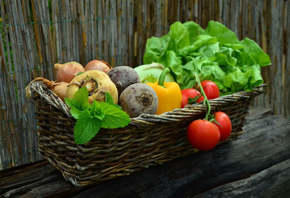 woven basket containing fruits and vegetables, wooden chair, fruits and vegetables in green, orange, yellow, and brown