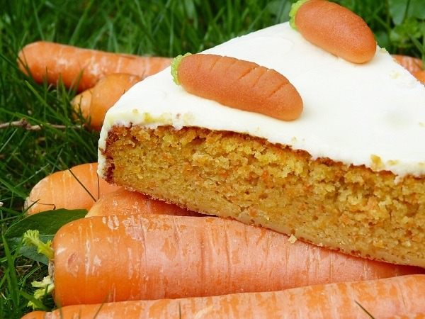 A slice of a carrot cake on top of carrot vegetables