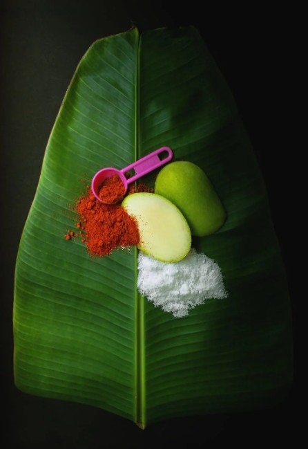 Mango cut in half on a big leaf with a spoon and some spices