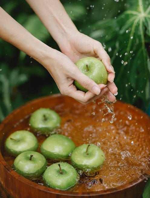 Woman washing green apples in a wooden bowl