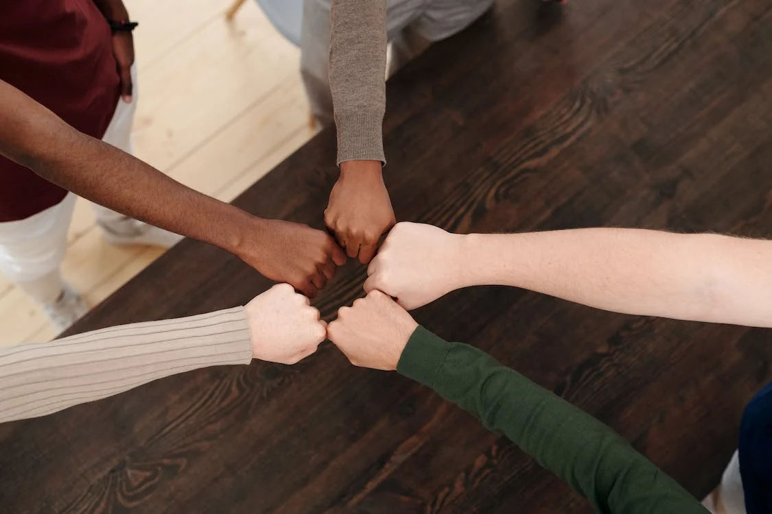 group of people doing fist bump with a wooden table on background