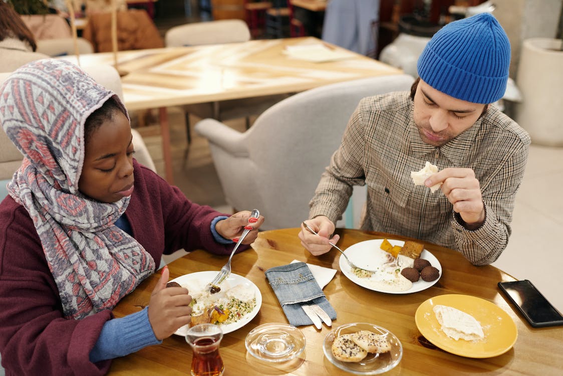 man with blue hat and woman eating on a table